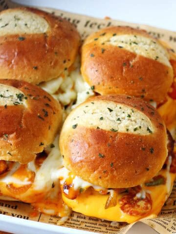 Chicken fajita sliders arranged in a baking dish with melted cheese, garlic butter–brushed brioche buns, and visible bell peppers.