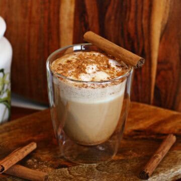 A glass of hot maple cinnamon latte surrounded by cinnamon sticks.