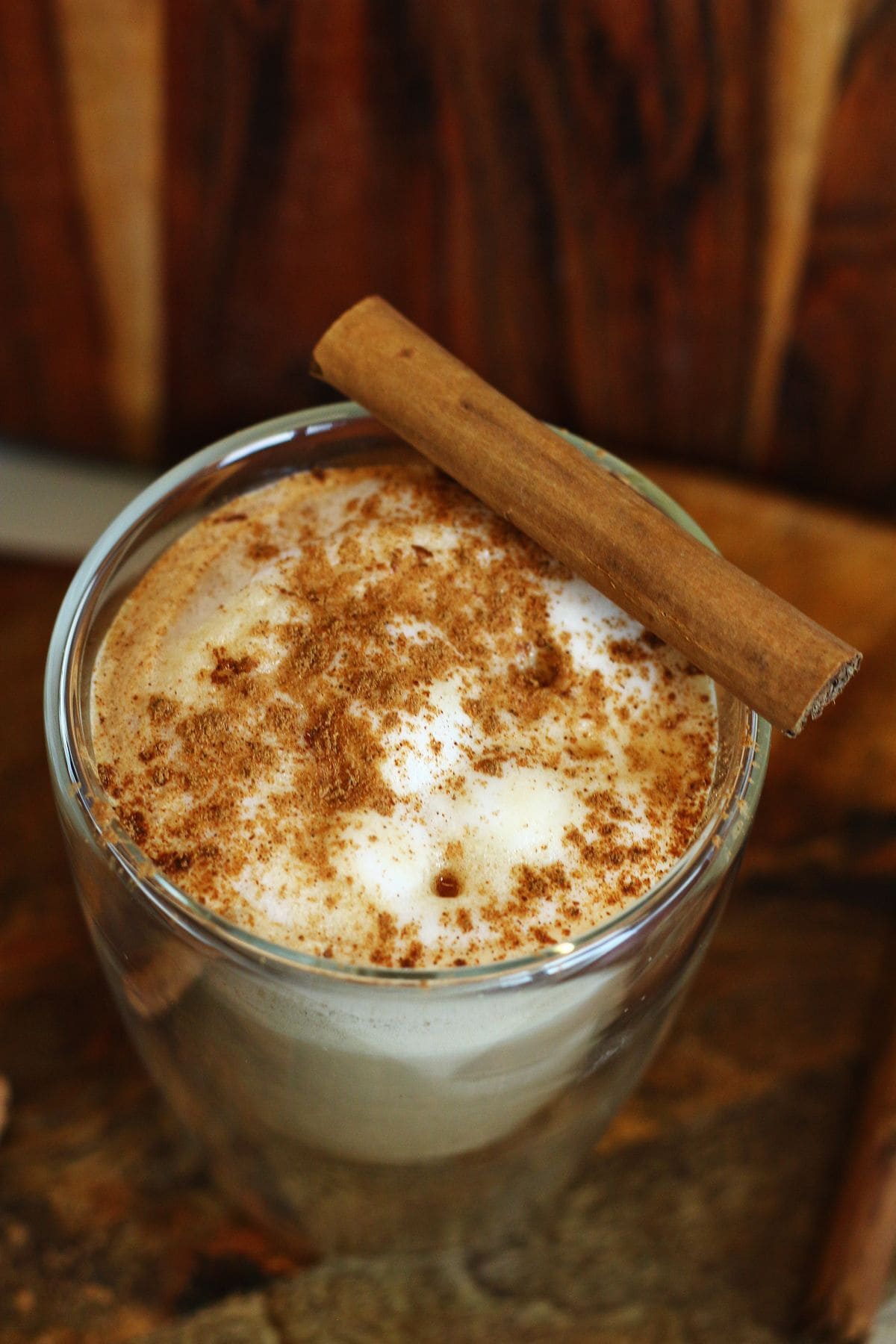 Close-up of a maple cinnamon latte with foamy milk and a cinnamon stick resting on top.