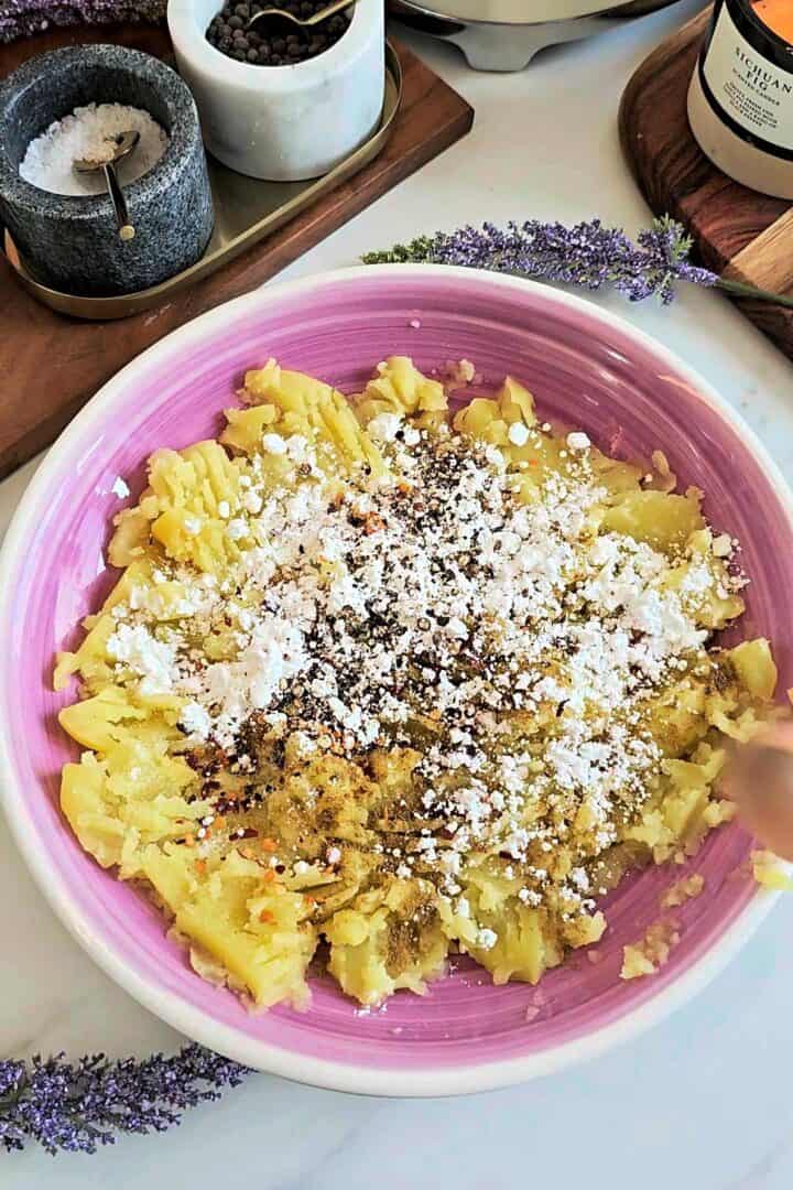 Mashed potatoes in a pink bowl topped with cornstarch and spices before mixing.