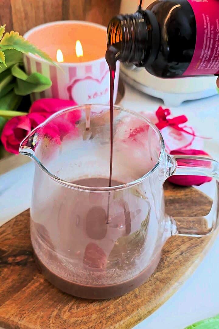 Vanilla extract being poured into a glass jug with hot chocolate mixture.