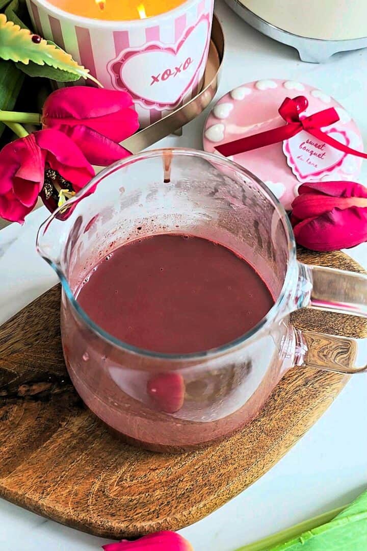 Red food coloring mixed into hot chocolate inside a clear glass jug.