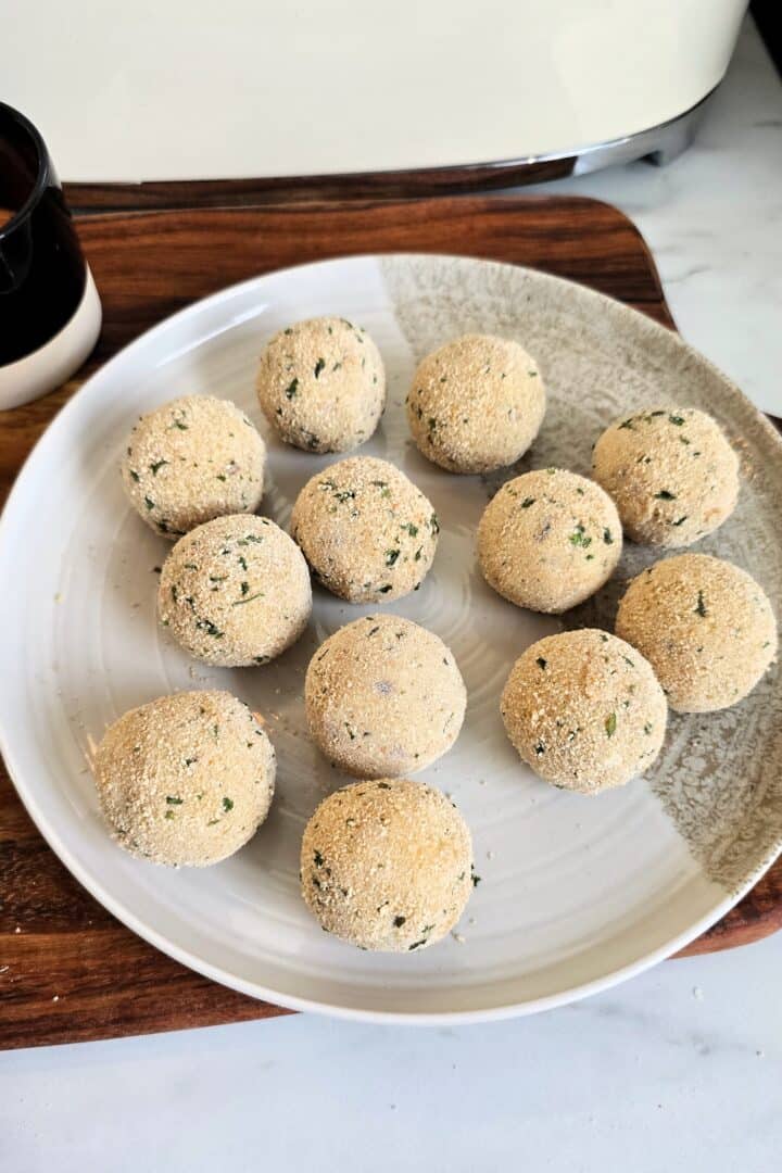 Plate of breadcrumb-coated potato balls arranged in a single layer before frying.