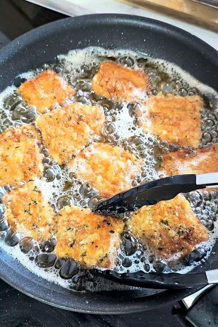 Breaded fish pieces frying in oil in a pan.