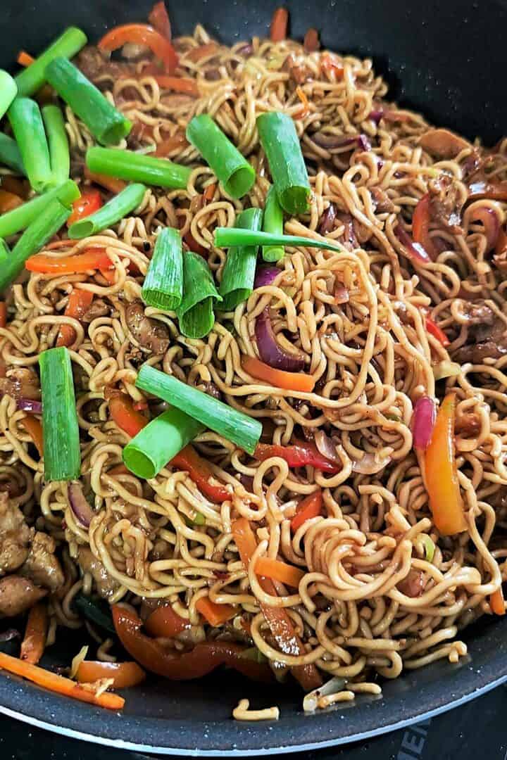 Chicken, vegetables, and noodles fully mixed together in a pan, topped with chopped green spring onions.