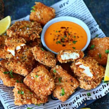 Breaded fish nuggets served with a bowl of sriracha dipping sauce and lemon wedges.