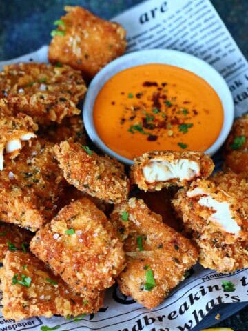 Breaded fish nuggets served with a bowl of sriracha dipping sauce and lemon wedges.