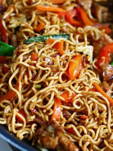 Close-up of chicken chow mein in a wok with glossy noodles, carrots, bell peppers, cabbage, and chicken pieces.