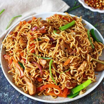 A mound of chicken chow mein with egg noodles, sliced vegetables, and chicken on a white rimmed plate.