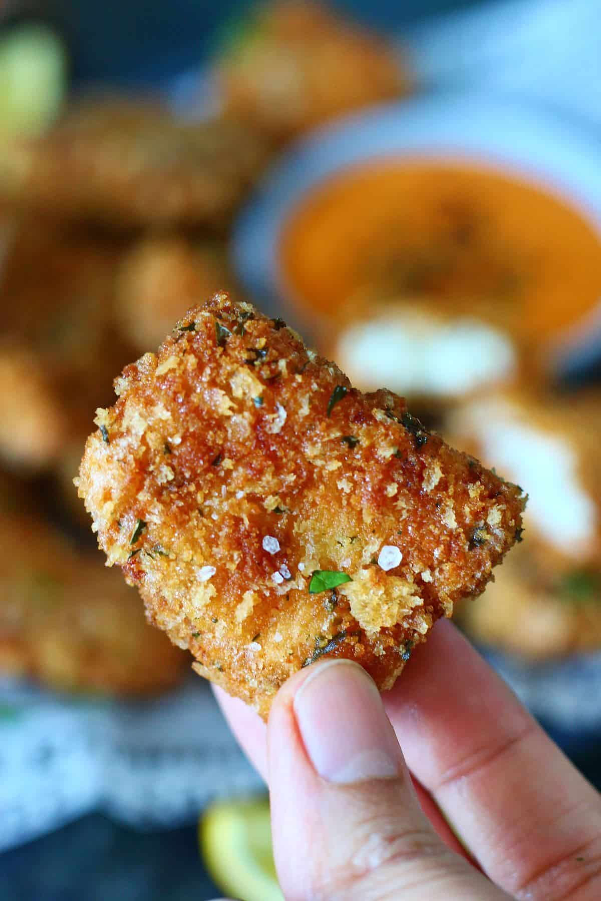 A hand holding a breaded fish nugget.