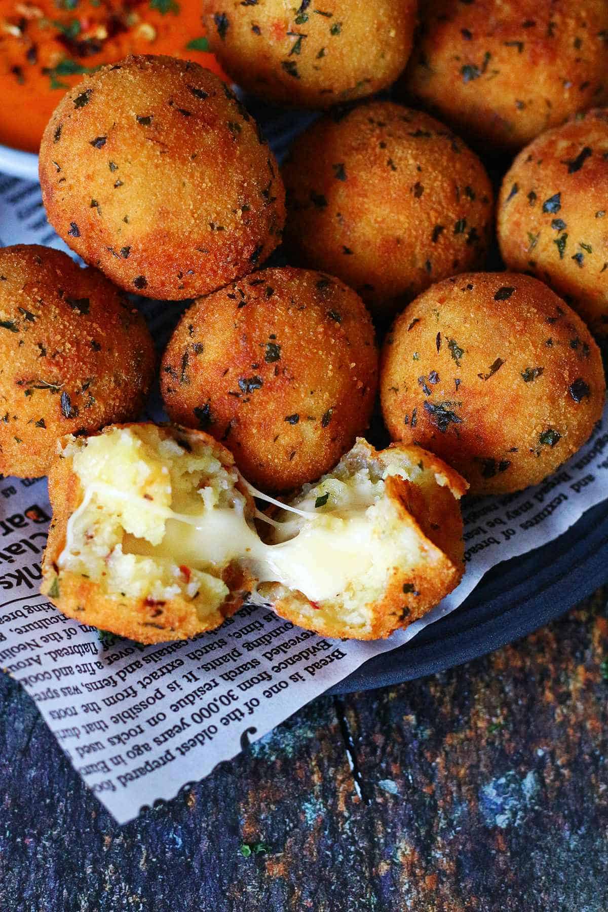 Close-up of golden fried potato and cheese balls on a plate, one cut open with melted cheese stretching out.