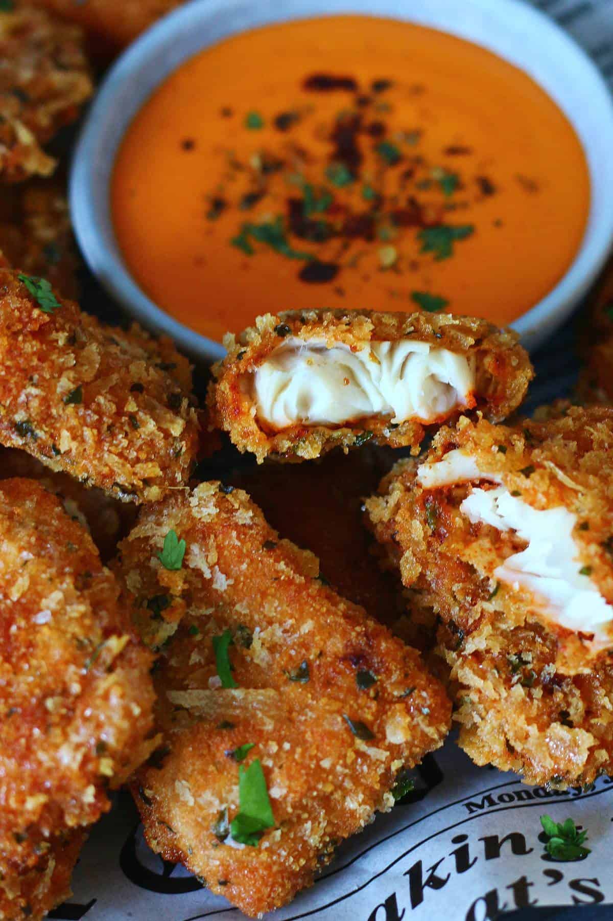 A close view of breaded fish nuggets arranged with a bowl of sriracha sauce.
