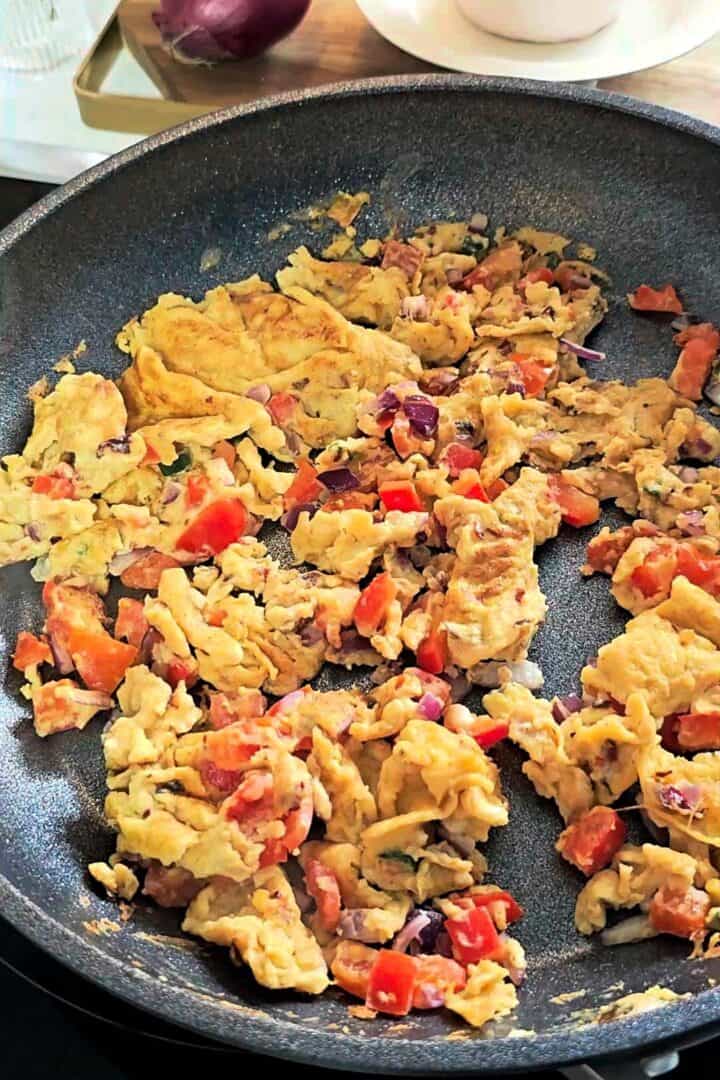 Scrambled eggs with diced tomatoes and onions cooking in a nonstick frying pan.