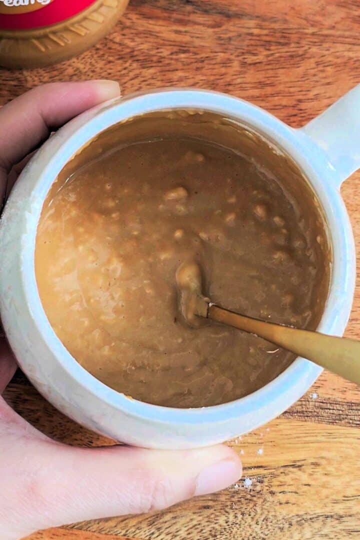 Biscoff mug cake batter being mixed in a white mug with a spoon.