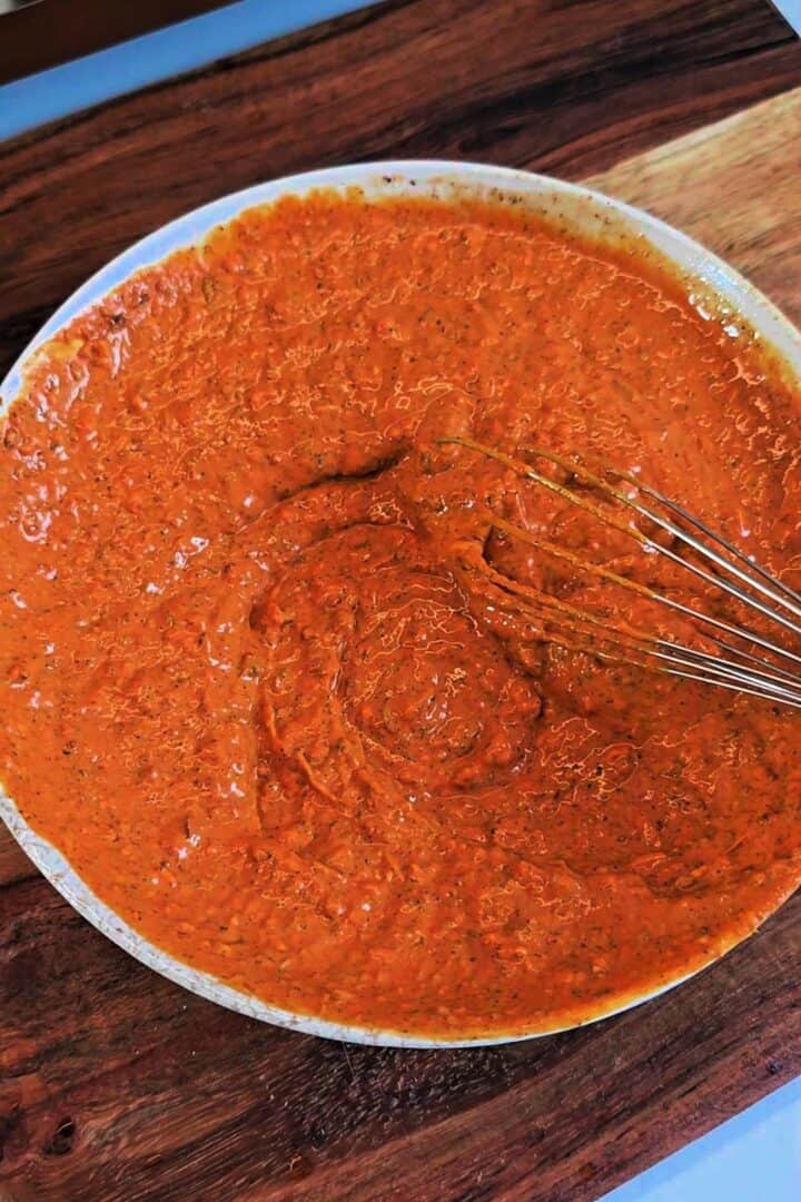 Spiced yogurt marinade being mixed in a shallow bowl with a whisk.