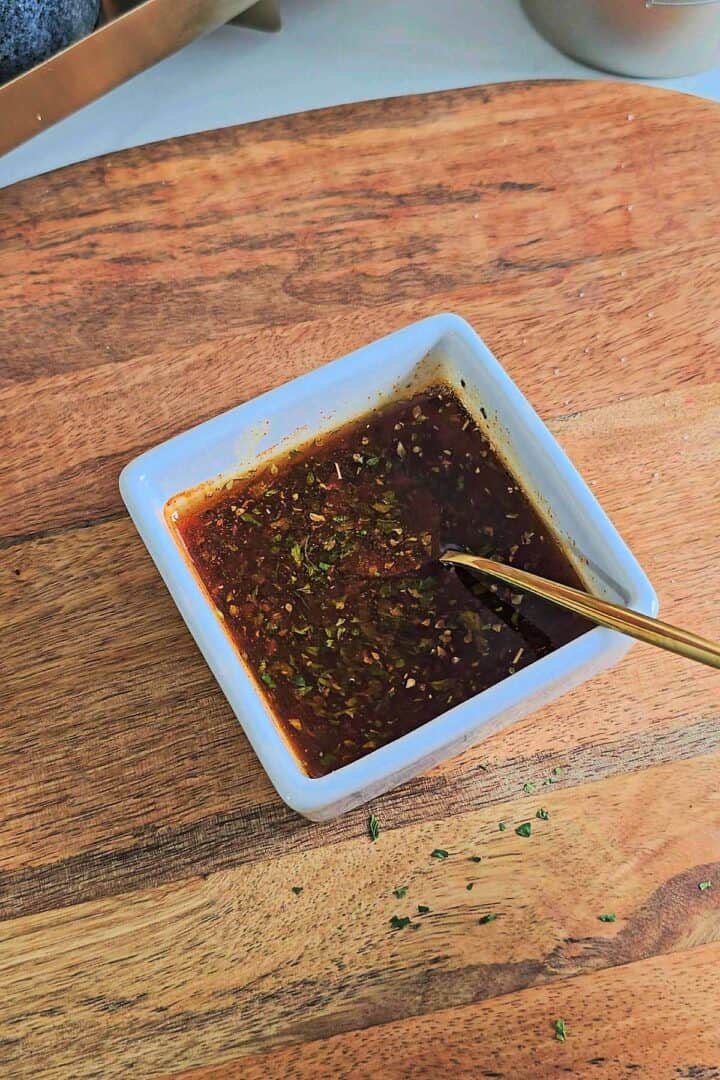 Small bowl of seasoning mixture with herbs and spices on a wooden surface.