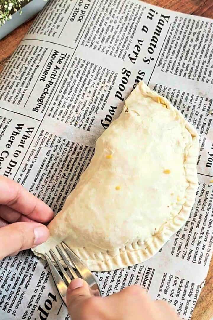Raw paratha folded into a half-moon pocket and sealed with fork marks on parchment paper.