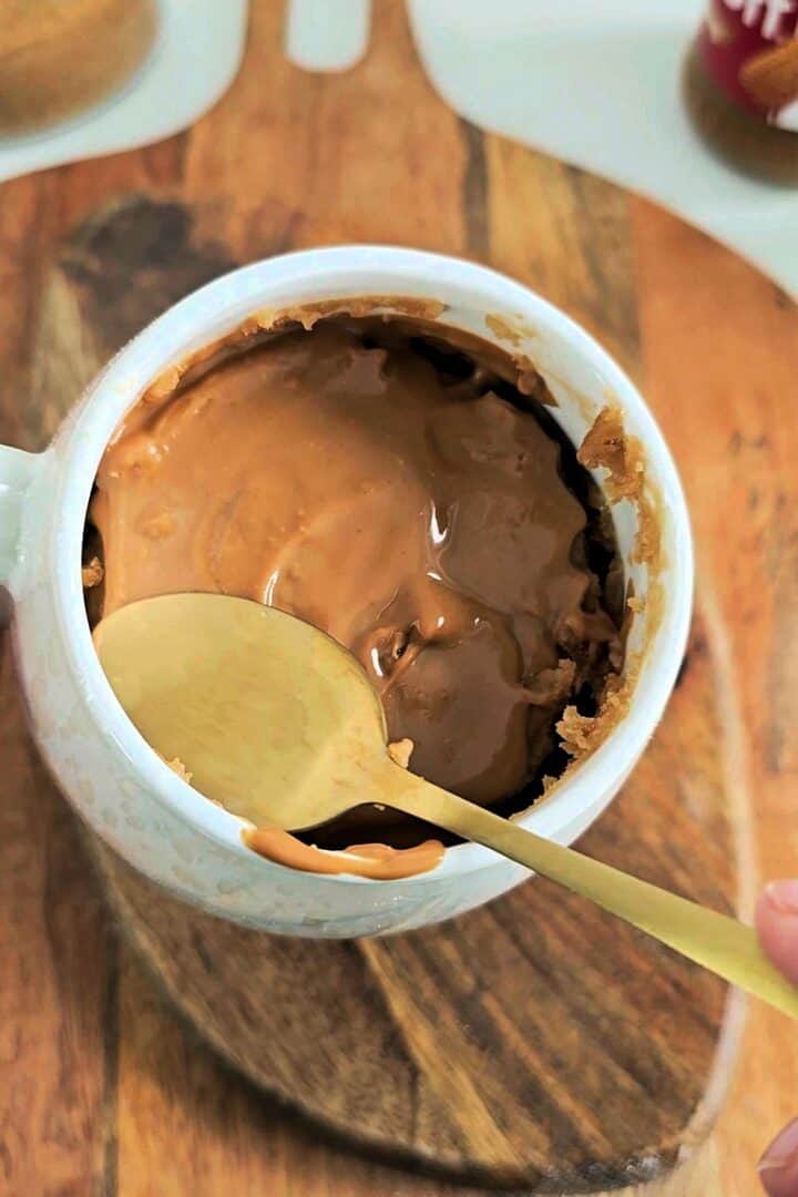 Biscoff spread melting over warm mug cake with a spoon inside the mug.