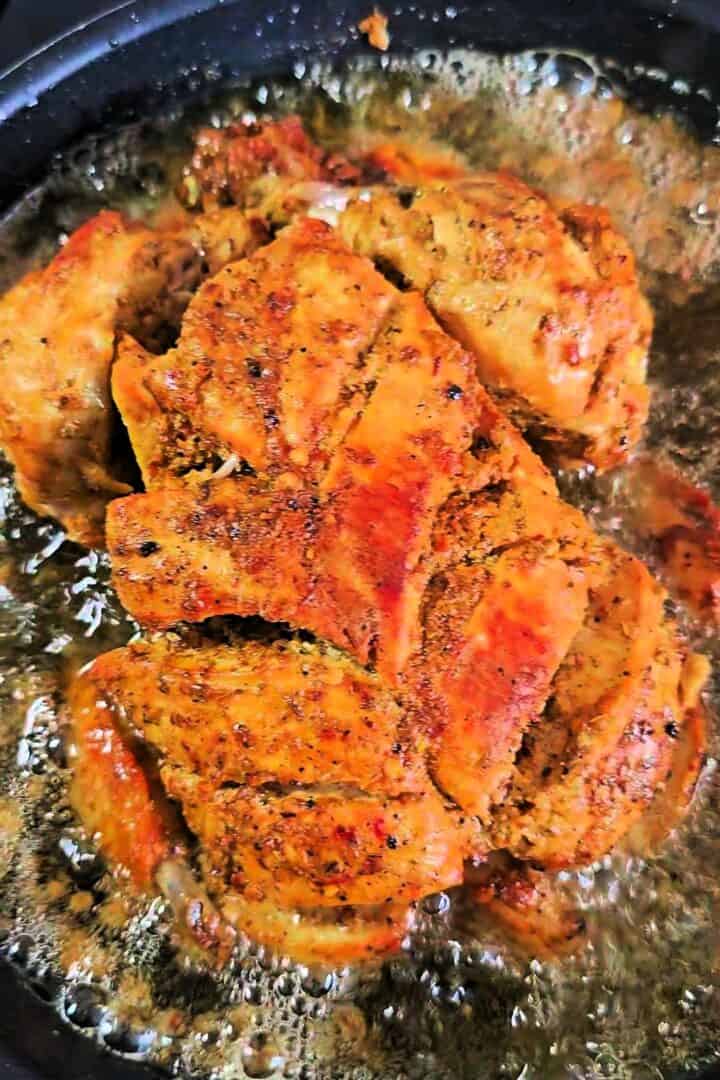 Whole chicken frying in hot oil in a pan.