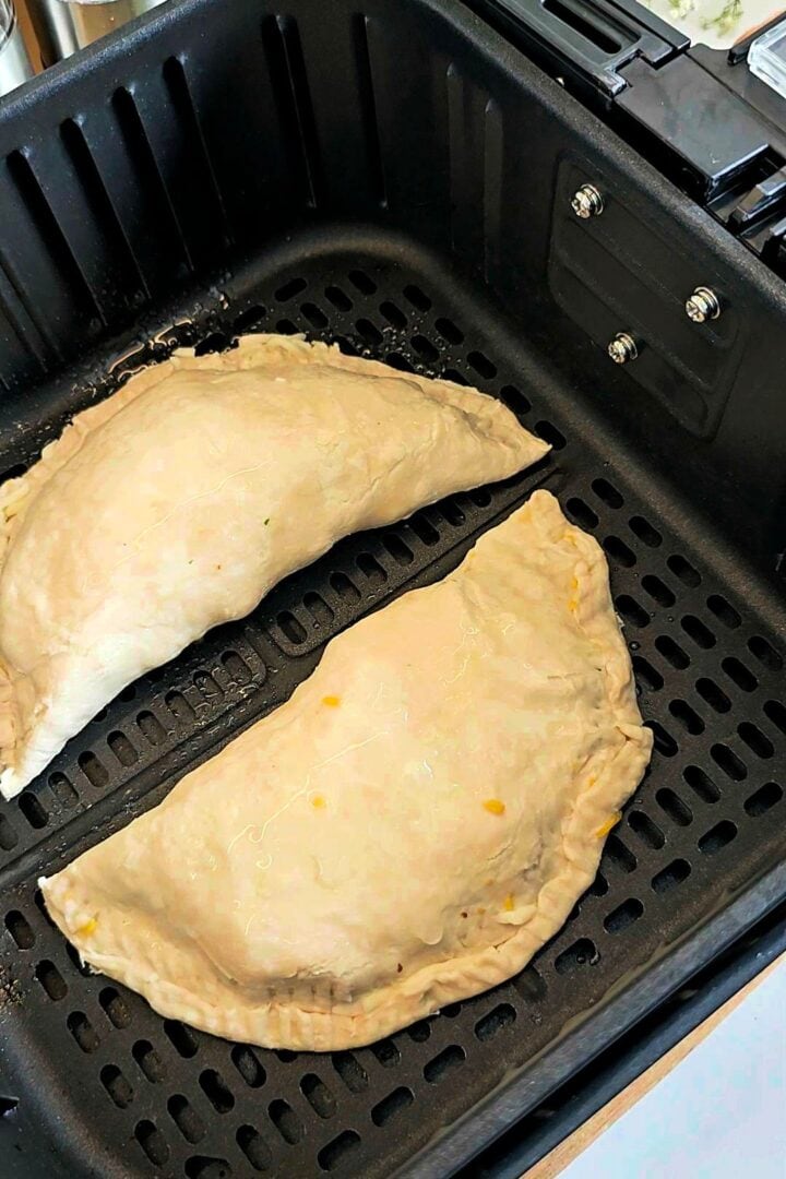 Two uncooked paratha pockets placed inside an air fryer basket.