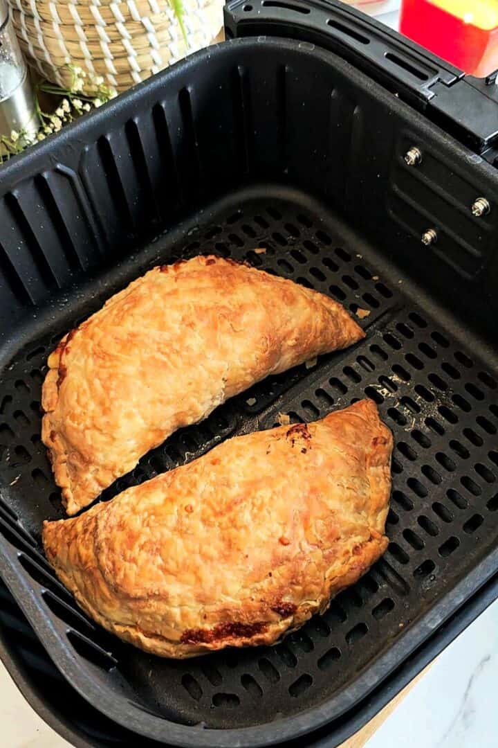 Two golden brown paratha pockets in an air fryer basket after cooking.