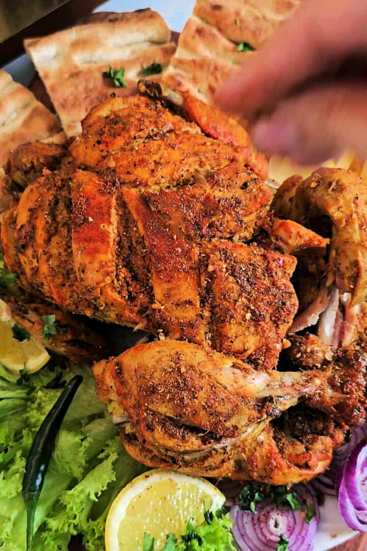 Fried chicken chargha on a platter with naan, lemon wedges, lettuce, and sliced red onions.