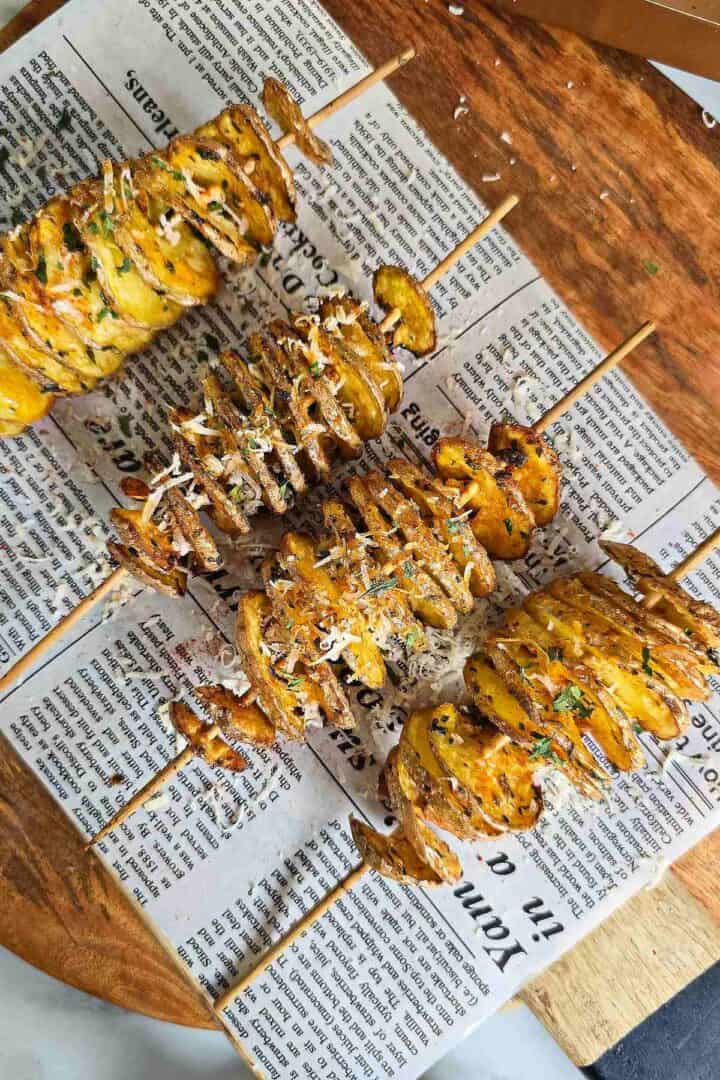 Finished tornado potatoes on skewers topped with grated parmesan and herbs on parchment paper.
