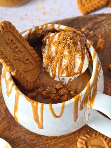 Biscoff mug cake topped with ice cream, Biscoff drizzle, and a whole Biscoff cookie on a wooden board.