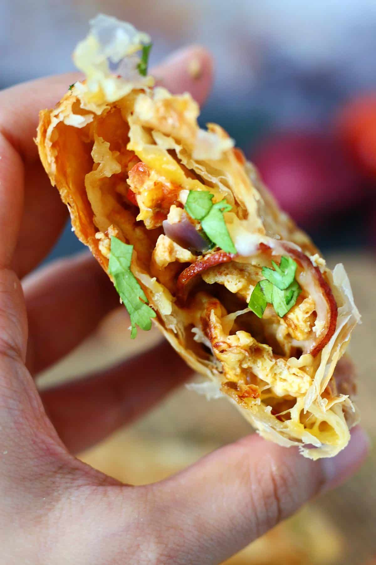 Hand holding a broken paratha pocket showing egg, bologna, vegetables, and melted cheese inside.