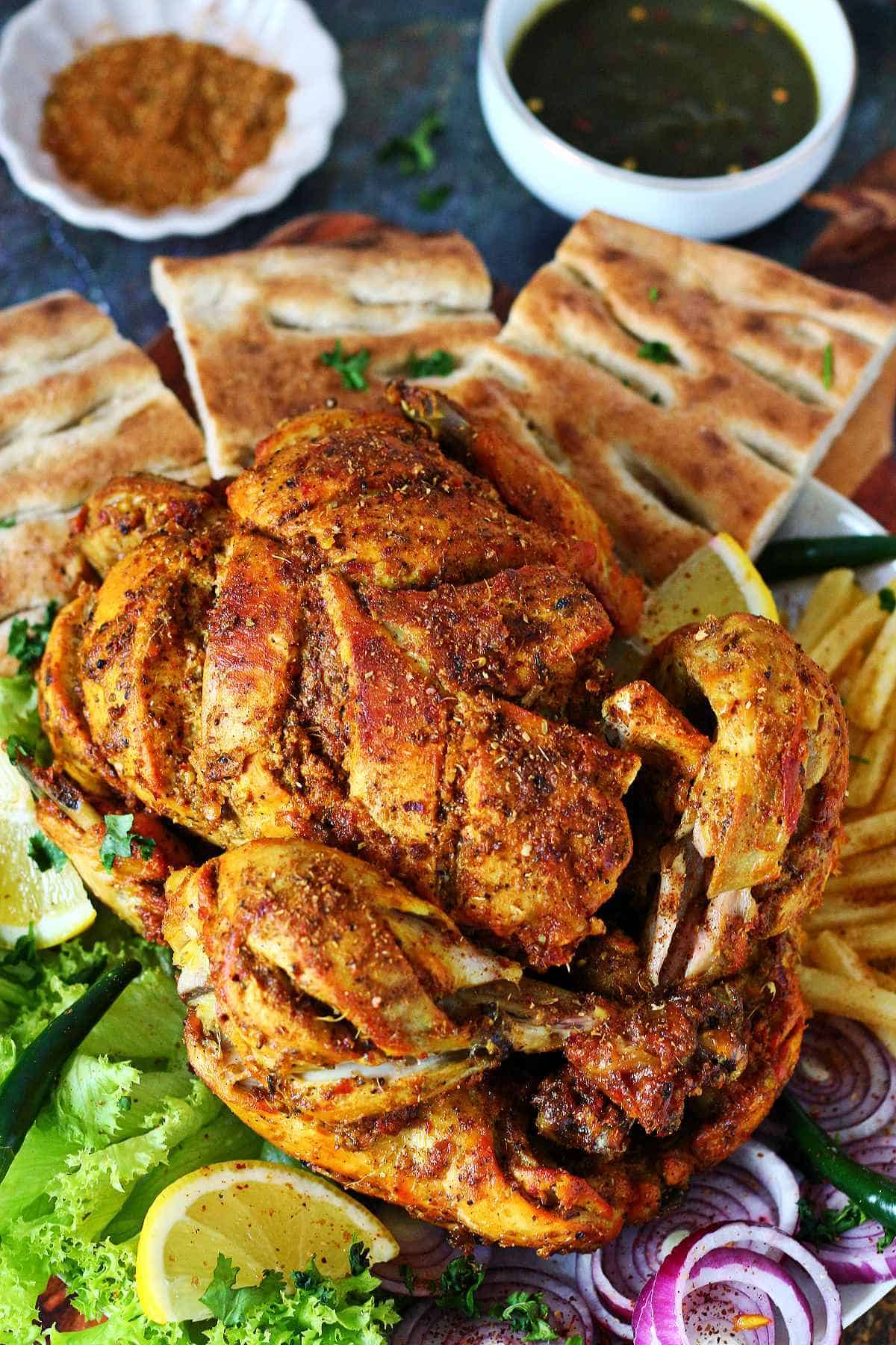 Whole lahori chargha served on a platter with naan, fries, lemon wedges, lettuce, and sliced red onions.