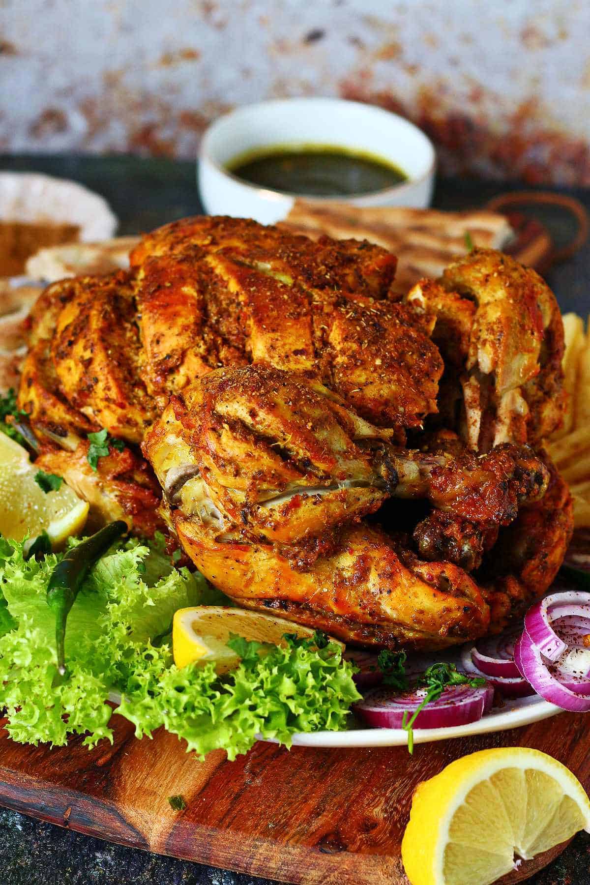 Chicken chargha on a serving platter with naan, fries, green chutney, and sliced onions.