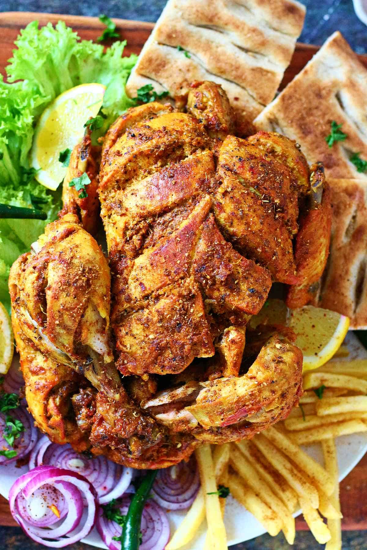 Overhead view of lahori chargha served with naan, fries, lemon wedges, and salad.