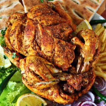Lahori chicken chargha plated with naan, fries, lemon wedges, and sliced onions.
