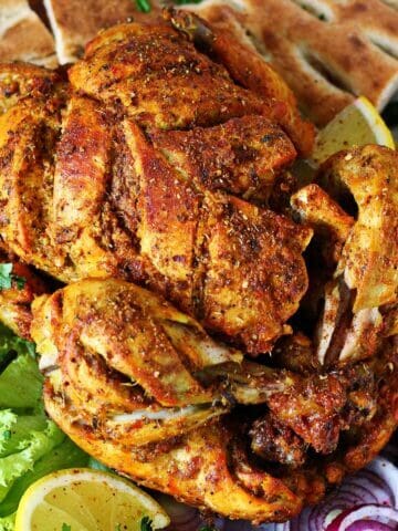 Lahori chicken chargha plated with naan, fries, lemon wedges, and sliced onions.