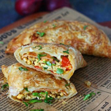 Two sliced paratha pockets stacked on parchment paper showing egg, bologna, vegetables, and melted cheese filling.