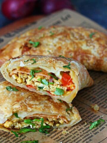 Two sliced paratha pockets stacked on parchment paper showing egg, bologna, vegetables, and melted cheese filling.
