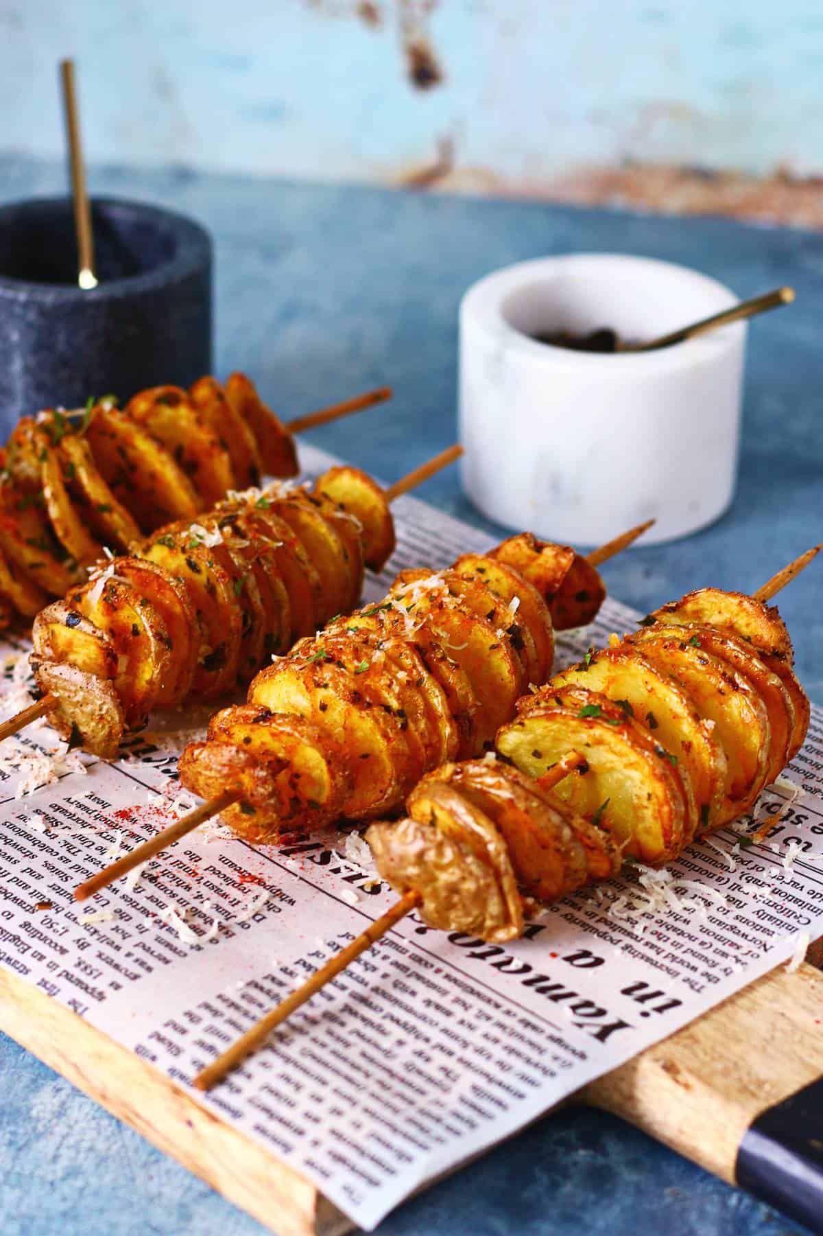 Multiple tornado potatoes on skewers arranged on a board lined with newspaper.