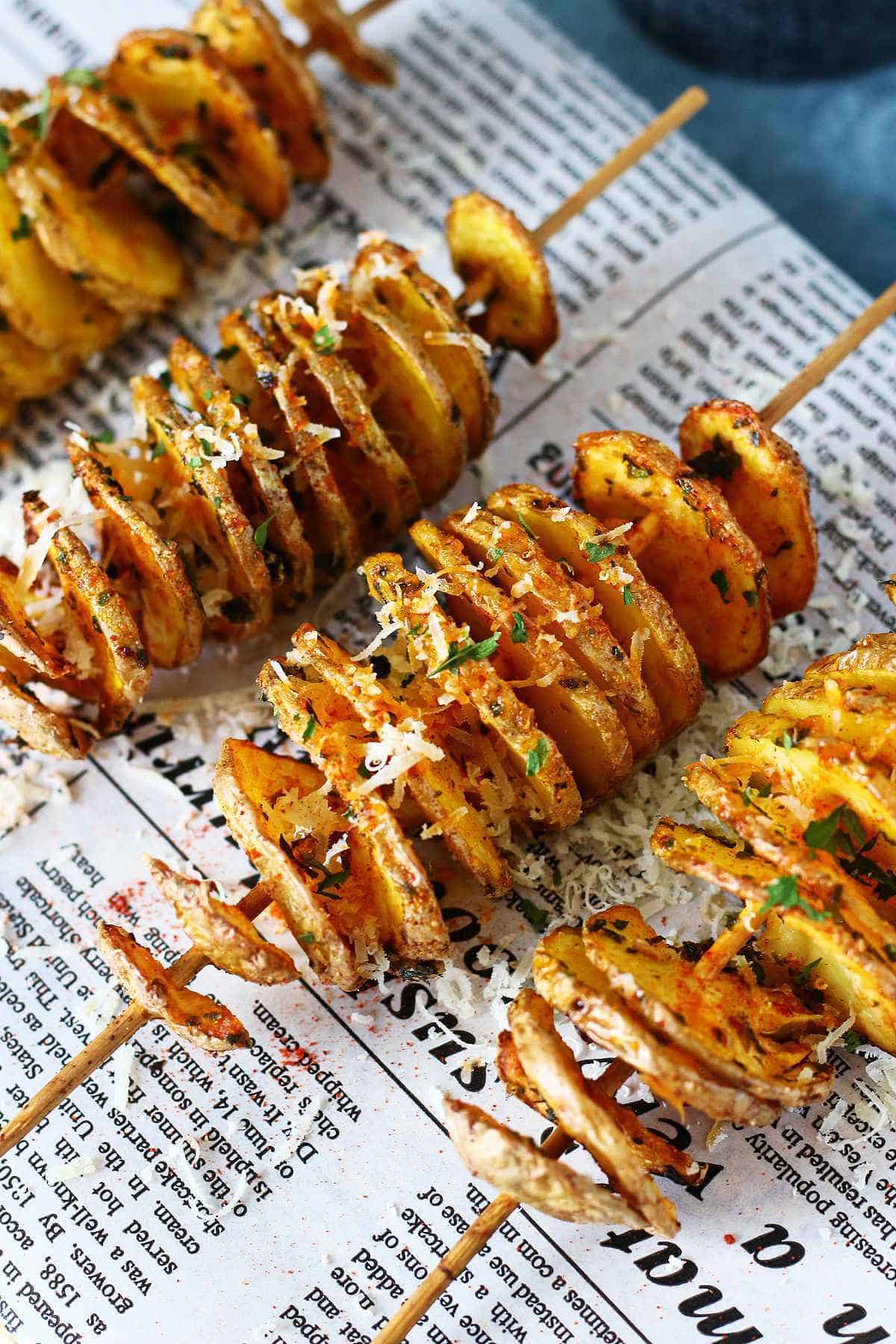 Air-fried tornado potatoes on skewers garnished with herbs and parmesan on parchment paper.