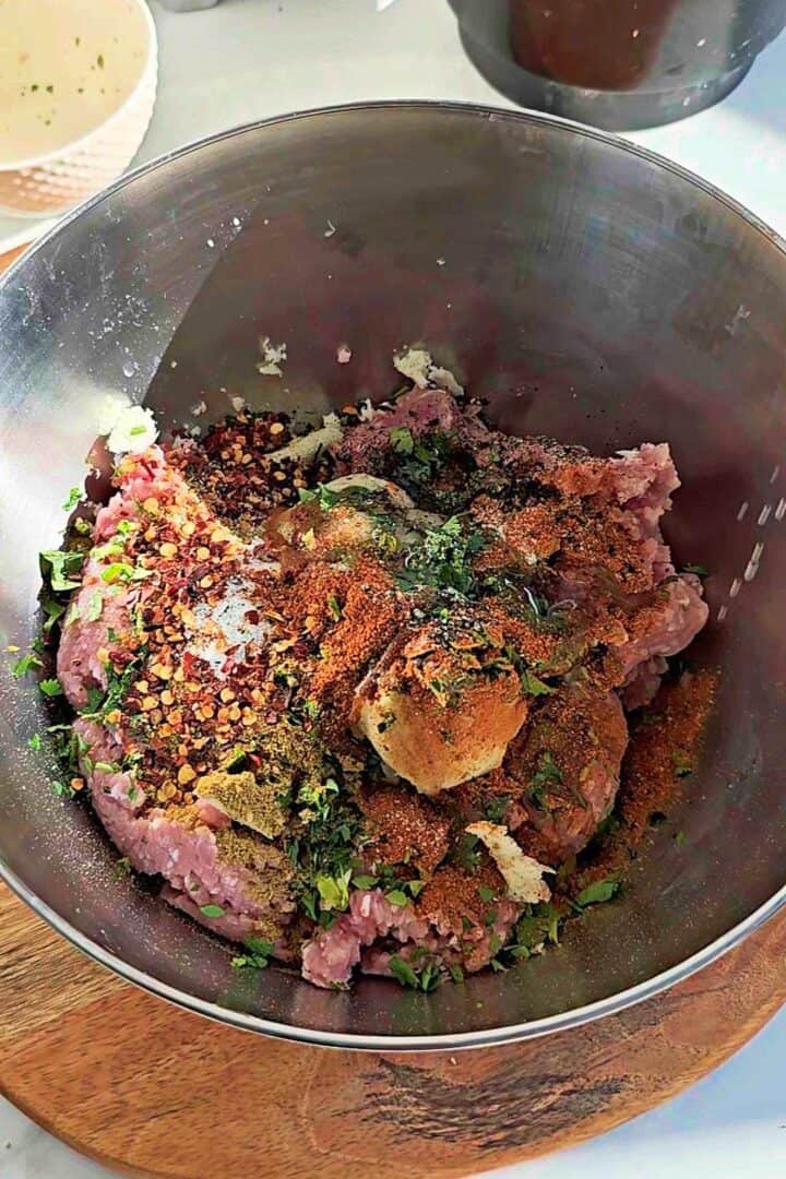 Ground meat with spices, herbs, onion, garlic, and ginger added in a mixing bowl.
