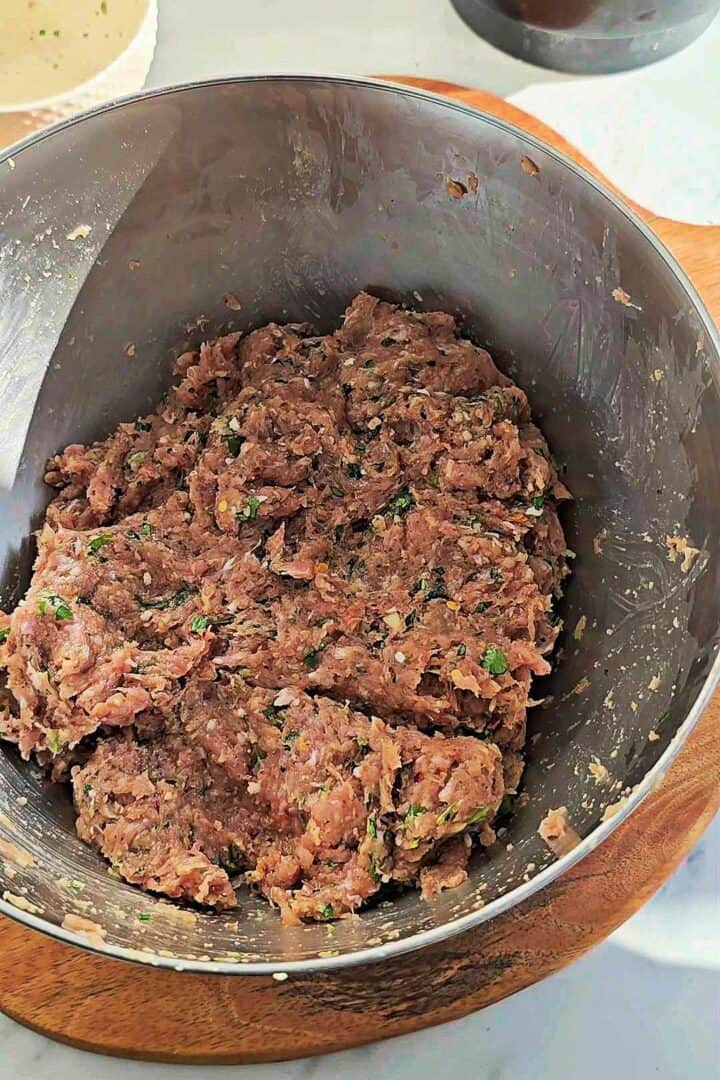 Kebab mixture kneaded until well combined and cohesive in a metal bowl.
