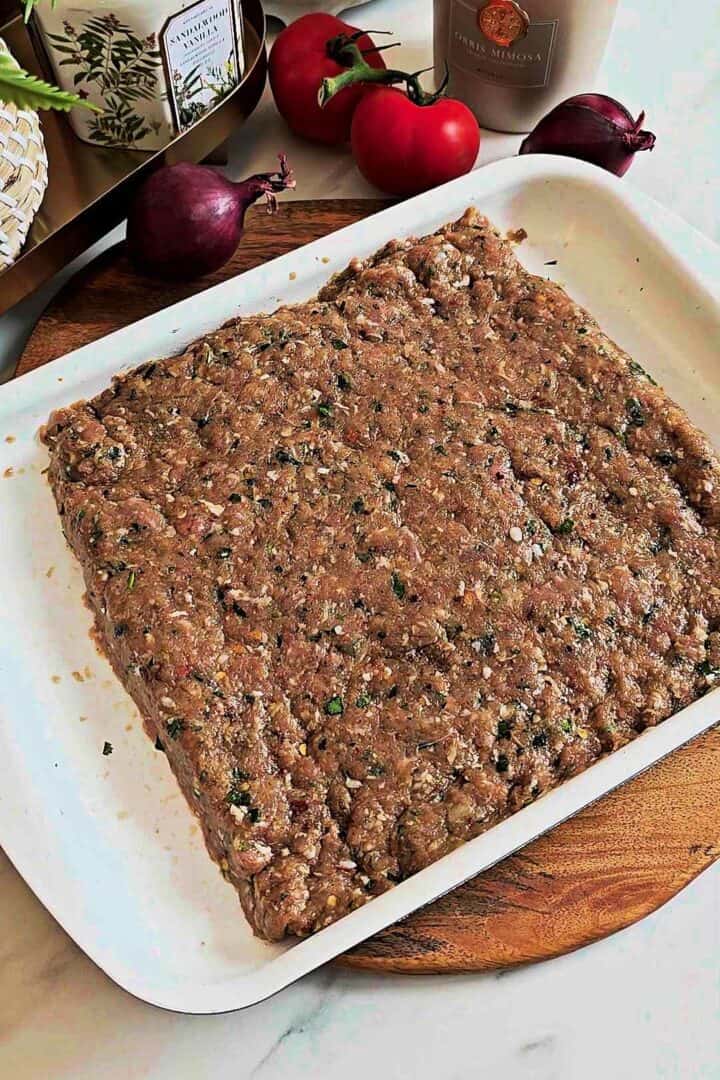 Ground meat mixture pressed into an even slab in a baking dish.