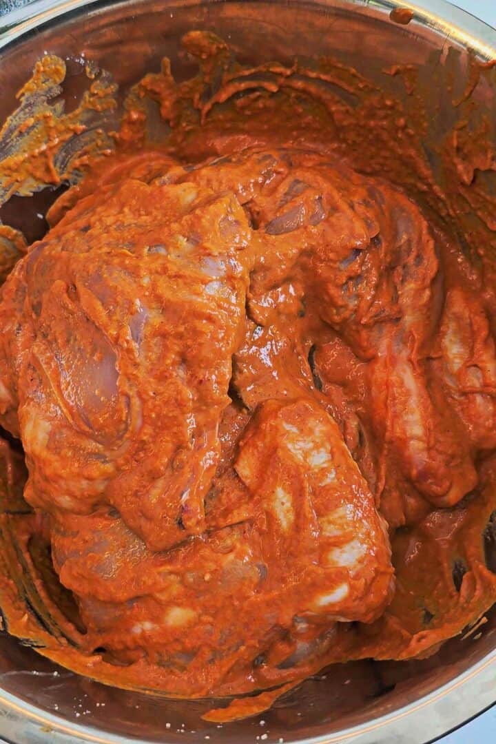 Chicken quarters coated in thick peri peri marinade in a mixing bowl.