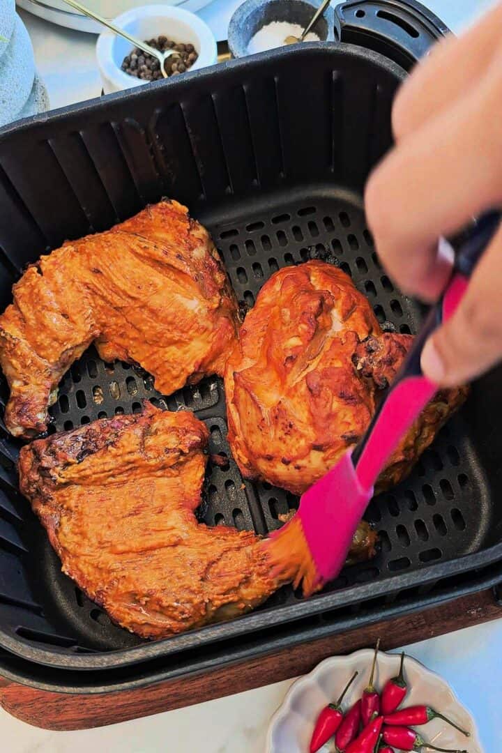 Basting peri peri chicken with sauce in an air fryer basket.