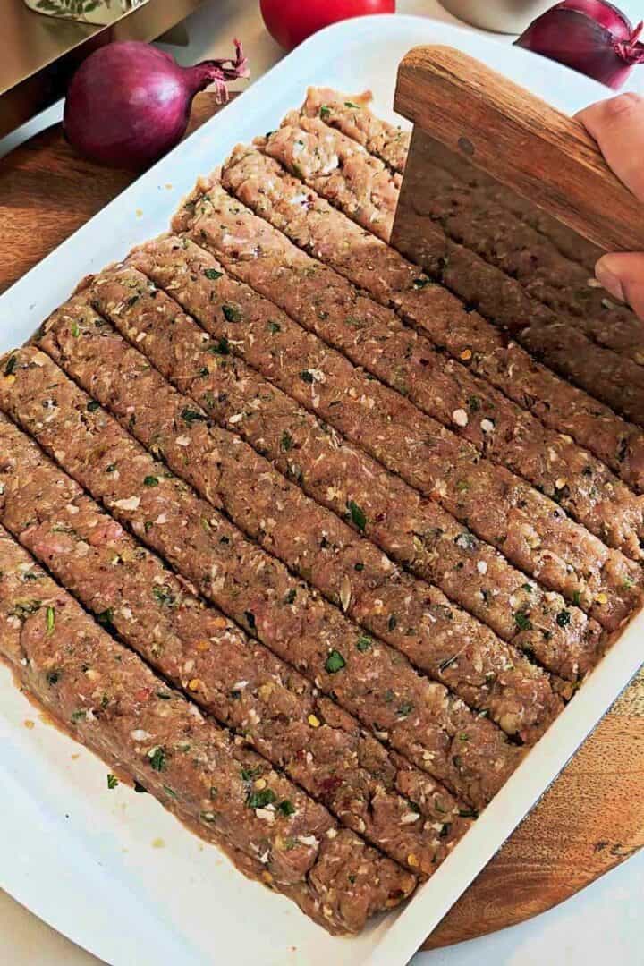 Raw kebab mixture cut into long strips using a dough cutter.