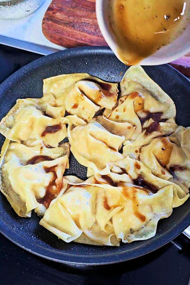 Sauce being poured over blanket dumplings in a pan.