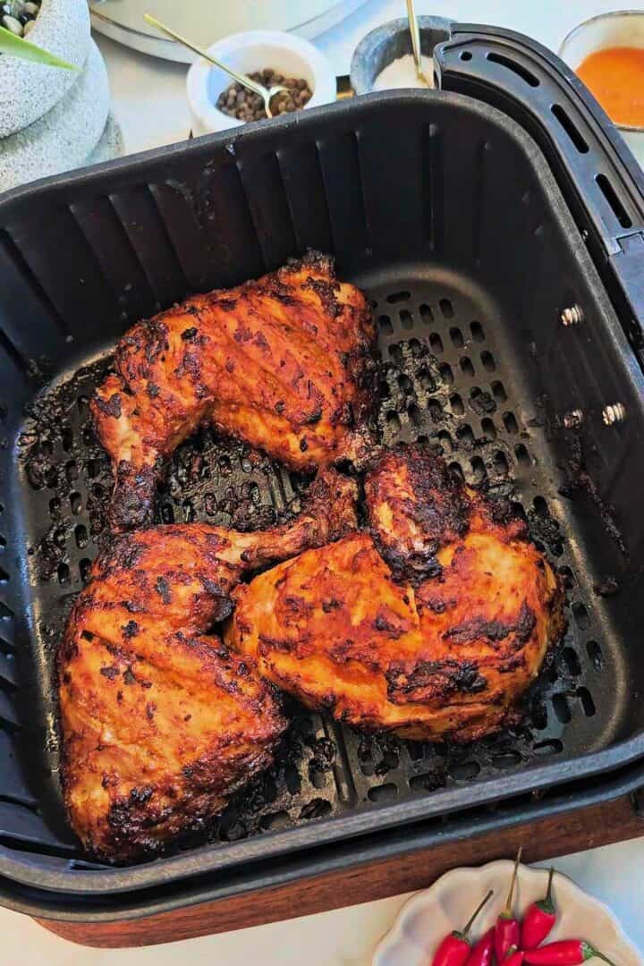 Charred air-fried peri peri chicken quarters in an air fryer basket after cooking.