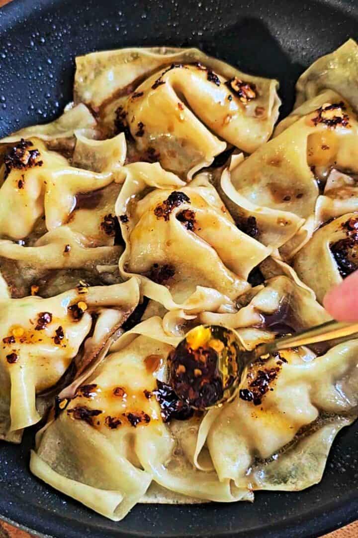 Chili crisp oil being spooned over cooked dumplings.