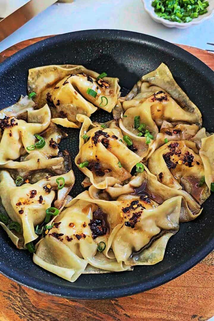 Dumplings garnished with chopped scallions in a pan.