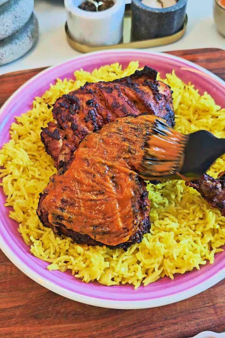 Brushing finishing peri peri sauce over cooked chicken served on yellow rice.