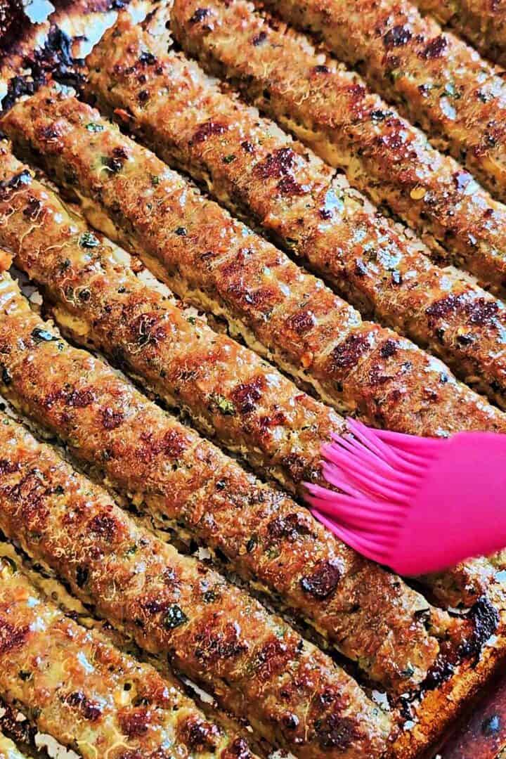 Butter being brushed over hot sheet pan kebabs with a pastry brush.